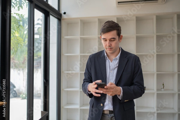 Obraz Happy business man talking on mobile cell phone device looking away standing at work, handsome businessman talking on his phone in office