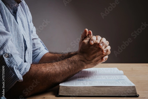 Fototapeta Man is praying with his hands together over the open bible, side view