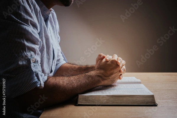 Fototapeta Man is praying with his hands together over the open bible, side view