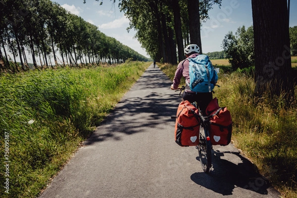 Fototapeta Frau radelt während einer Radreise auf einem Radweg entlang eines Kanals in Flandern, Belgien