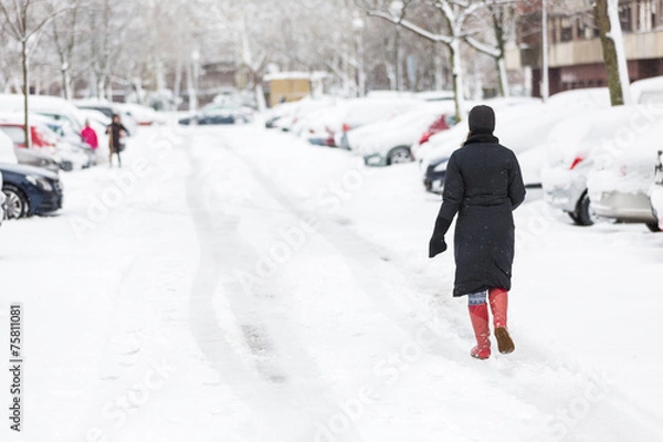 Obraz Woman dressed in black coat and boots walking alone on the snow