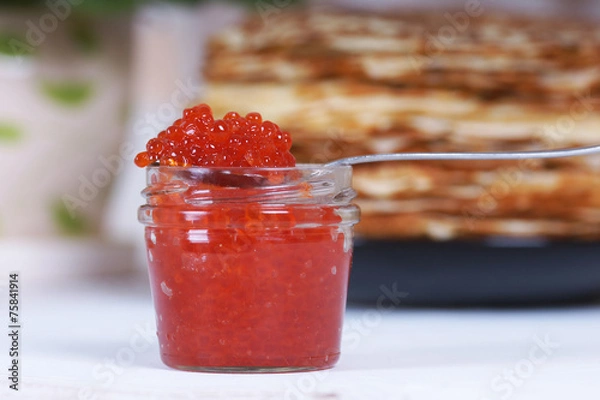 Obraz Банка красной икры на фоне большой стопки блинов на столе