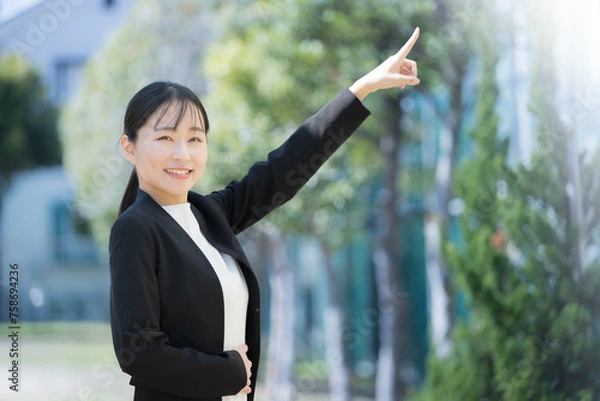Fototapeta 目標や未来に向けて指を差すビジネスウーマン　都会のビルなどの背景　就職や採用、転職のイメージ