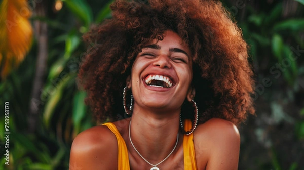 Obraz A radiant woman with a bright smile and voluminous curly hair enjoys a moment of genuine laughter amidst lush tropical greenery. This image captures the carefree joy and vitality of youth