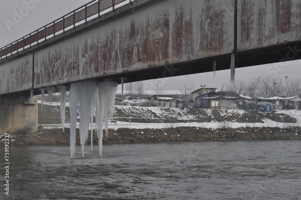 Fototapeta Large pieces of icicles hang from the lower part of the metal bridge over the Vardar River in Skopje.
