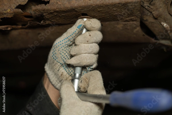 Fototapeta A mechanic in a hole under a car unscrews nuts in a garage while repairing a car. The mechanic unscrews the nuts removing the protection from the car to drain the old oil from the car.