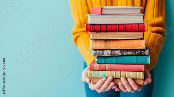 Fototapeta Woman hands holding pile of books over light blue background. Education, library, science, knowledge, studies, book swap, hobby, relax time