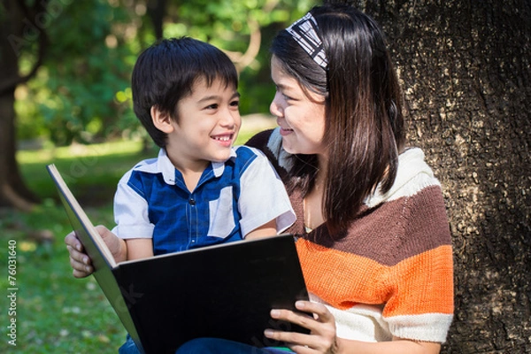 Fototapeta Mother reading a book with her son with smile face in park under