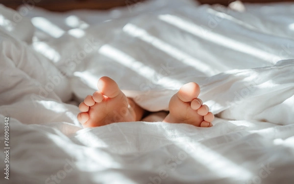 Fototapeta Cute feet of little sleeping child sticking out from under the blanket at sunny morning