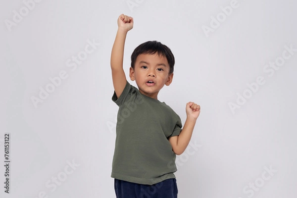 Fototapeta Excited 2-3 years old Asian boy wearing a green t-shirt looking at the camera while doing winner gesture isolated on white background