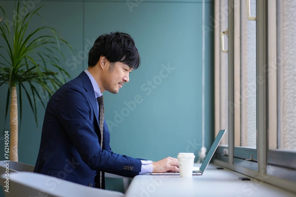 Fototapeta グリーンのオフィスとスーツとPCの男性