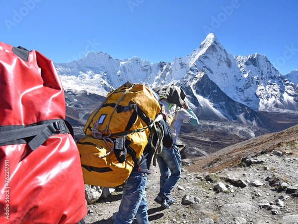 Fototapeta The adult sherpa porters carrying heavy backpacks and sacks in the Himalayas at Nepal, in the background the mountain of Ama Dablam