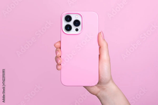 Obraz iPhone 15 Pro in female hand in pink silicone cover isolated on pink background phone case mock up in monochrome colours back view