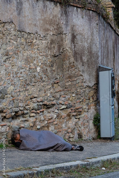 Fototapeta Homeless man sleeping on a street, by the parking and begs for help and money. The problems of large modern cities.