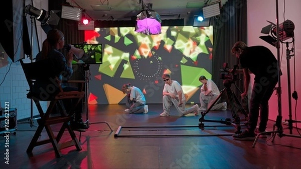 Fototapeta Backstage video shoot. Two girls and a guy dancing against a big LED screen with bright backgrounds.