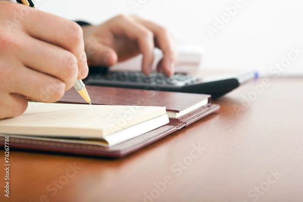 Fototapeta Businessman using a calculator on a wooden desk.