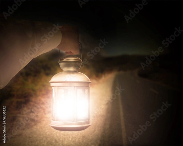 Fototapeta Hand holding light illuminating dark road at night