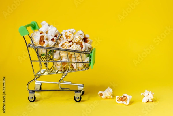 Obraz Freshly made popcorn on yellow background in a shopping cart