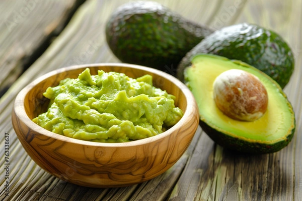 Obraz Halved avocado and guacamole in wooden bowl for healthy food concepts.