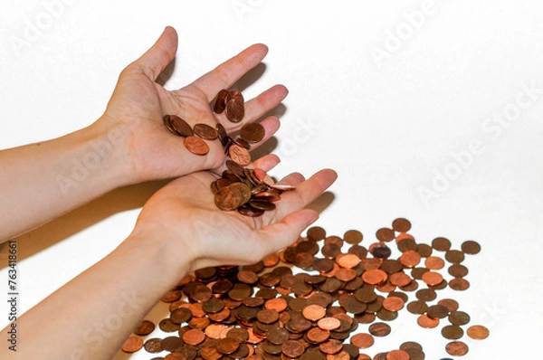 Fototapeta Two hands holding some pennies while multiple pennies are on a white backdrop
