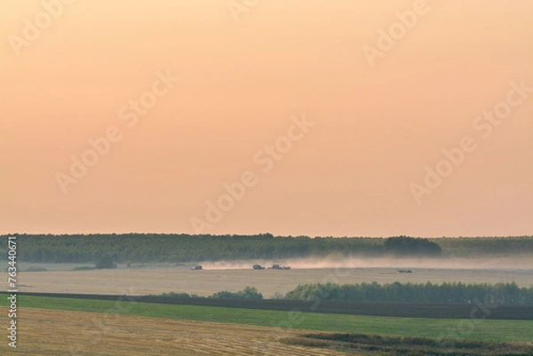 Fototapeta harvesters in in the distant fields in the evening