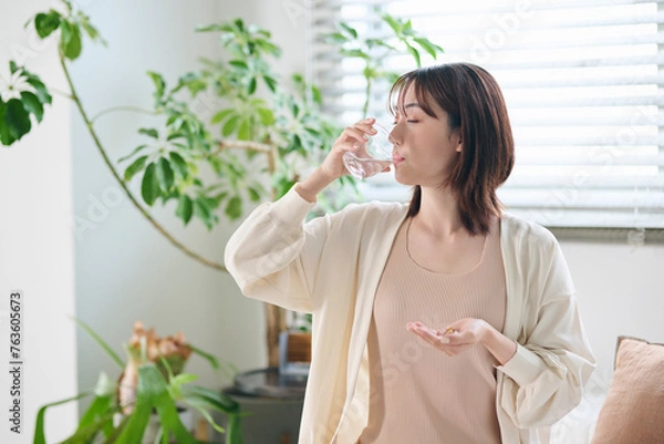 Fototapeta ベッドでサプリを飲む20代女性