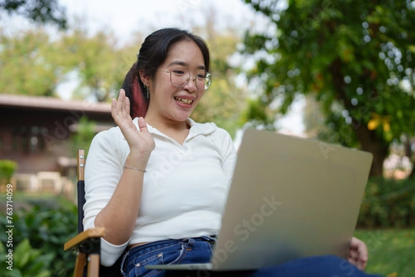 Fototapeta Young women wearing glasses wearing headphones reading a book Making diary notes Video calls via laptop online, relaxing, lifestyle, vacation, at the park Happily natural place.