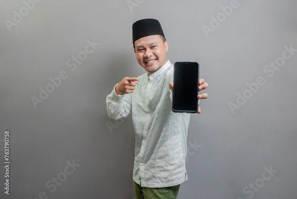 Fototapeta Portrait of an Asian Muslim man smiling with pointing finger to his smartphone