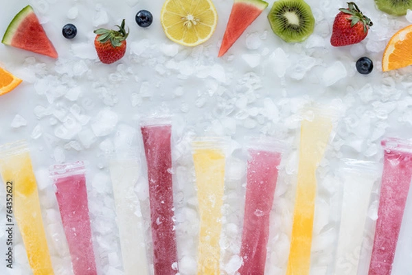 Fototapeta A row of DIY freezies with a border of fresh fruit pieces and ice all around.