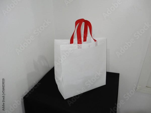Fototapeta Beautiful Non Woven grocery shopping white bag with red handle loop isolated on black table against white wall background