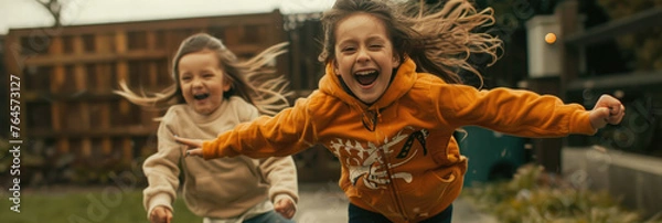 Fototapeta Two young girls, full of energy and joy, are running down a sidewalk together. They are laughing and enjoying their time outdoors