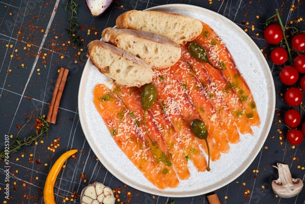 Obraz Salmon carpaccio with herbs, on a plate, on a dark background