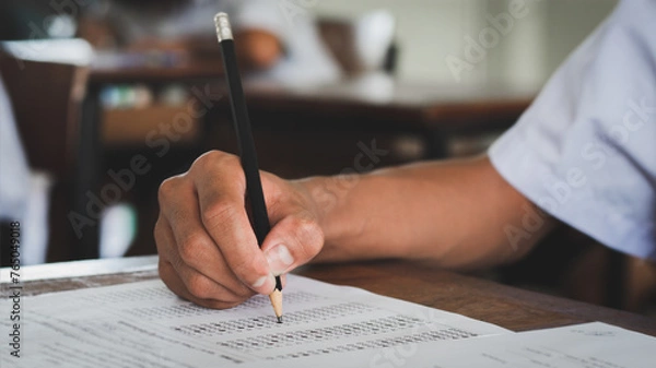 Fototapeta Close up hand of students reading and taking exam sheets exercises answer with stress in classroom.