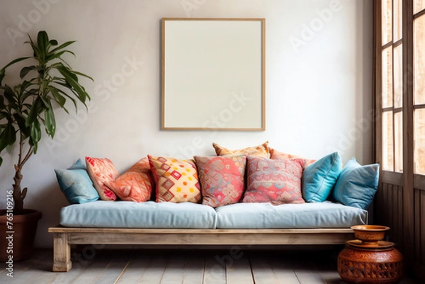 Fototapeta Cozy bohemian eco living room with wooden window, patterned multi-colored pillows on the soft sofa and framed mock up on the light wall. Modern interior design with copy space