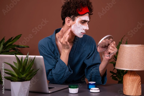 Fototapeta Funny man with cream on his face. Spa treatments. Skin care. Morning procedures before starting work. Brown background. The guy is looking at the camera.