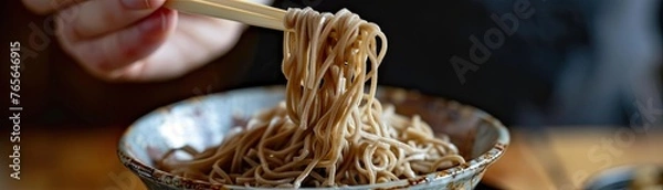 Obraz Action shot of soba noodles being lifted from a bowl with chopsticks emphasizing the texture and heartiness of the dish