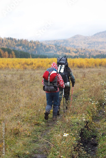 Fototapeta Two hikers with backpacks exploring a grassy field under the open sky