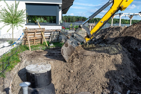 Obraz Using an excavator to bury a 10 m3 concrete septic tank located in the garden next to the house.