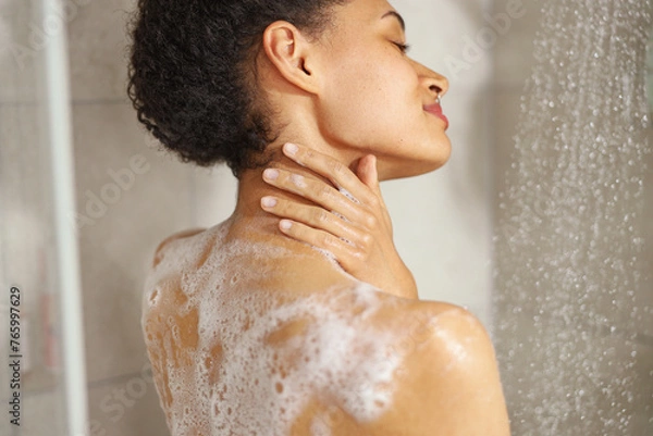 Fototapeta A woman lathers soap on her shoulder while taking a shower