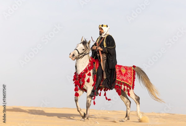 Fototapeta Saudi Man with his white stallion in a desert, shooting an arrow