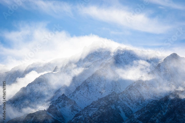 Fototapeta A closeup view of a mountain peak covered in snow as the wind swirls clouds around it. Aspen Springs, California - Highway 395