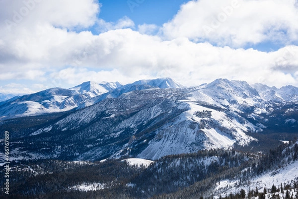Fototapeta A view of snowy mountains and puffy clouds on a sunny winter day in Mammoth Lakes, CA