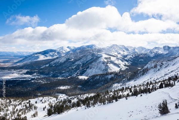 Fototapeta A view of snowy mountains and puffy clouds on a sunny winter day in Mammoth Lakes, CA