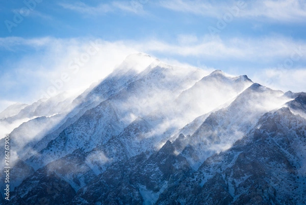 Fototapeta A closeup view of a mountain peak covered in snow as the wind swirls clouds around it. Aspen Springs, California - Highway 395