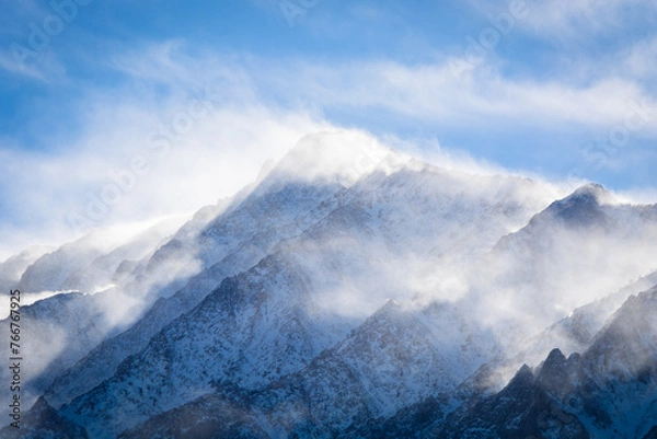 Fototapeta A closeup view of a mountain peak covered in snow as the wind swirls clouds around it. Aspen Springs, California - Highway 395