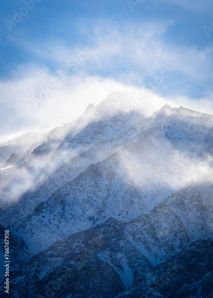 Fototapeta A closeup view of a mountain peak covered in snow as the wind swirls clouds around it. Aspen Springs, California - Highway 395
