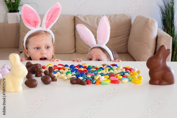 Obraz Cute children, kids with rabbit ears hunt looks in surprise at the chocolate eggs on the table