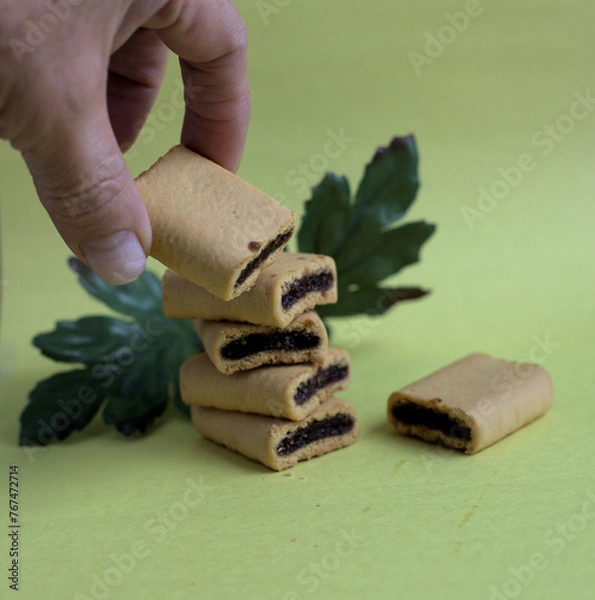 Obraz Hand holding a fig bite with a green leave on a yellow background.