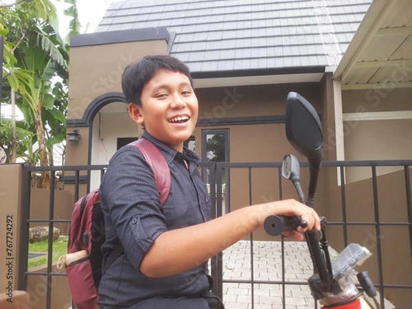 Obraz an elementary age school boy with his bag pack in front of the house use electric bicycle ready go to school