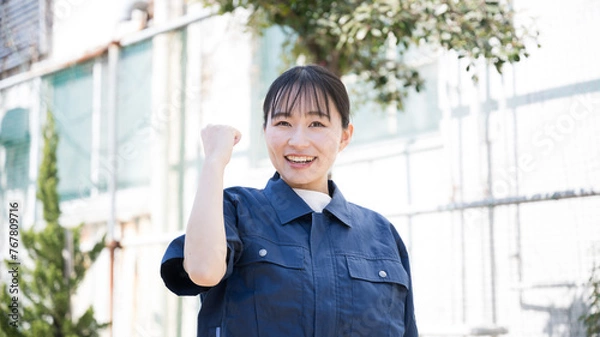 Fototapeta 工場のような背景で製造業などの作業着を着た女性のイメージ　ガッツポーズ